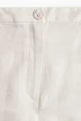 Pantalón sastrero color crema en tejido liviano de mezcla de lino y viscosa con pinzas adelante y atrás. Modelo de tiro alto con cierre, botón nacarado y piernas amplias.