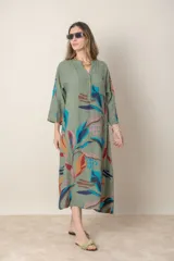 Vestido largo de lino color verde militar con estampado de hojas en tonos azul, naranja y marrón. Tiene cuello mao con botones, mangas tres cuartos y un bolsillo en el pecho.