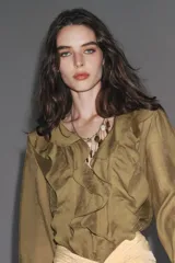 Camisa color verde oliva de tela traslúcida, con escote en V y volantes en el frente y cuello. Mangas largas abullonadas con puños elásticos.
