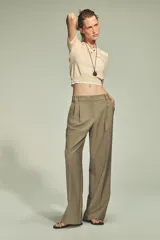Pantalón color arena de tiro alto con trabillas, bolsillos laterales y falsos bolsillos de vivo en la espalda. Presenta detalle de pliegues y cierre frontal con cremallera, botón interior y gancho metálico.