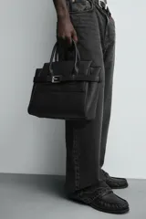Bolso bandolera negro con detalle de cinturón, compartimento principal con cierre mediante doble imán, bolsillo interior con cierre mediante cremallera, dos asas de mano y un asa de hombro ajustable y extraíble.
