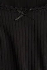 Remera negra de manga larga, corte ajustado y corto (cropped), confeccionada en tejido de punto acanalado. Presenta un escote redondo ribeteado con encaje y un pequeño lazo de satén en el centro del escote.