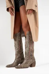 Botas texanas de cuero color marrón con bordados de estrellas y rayos de sol en color blanco. Presentan detalles en rojo en los bordes superiores y un taco de madera. El largo de la caña es de 42cm y la circunferencia de 37cm.