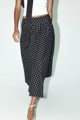 Falda midi negra con estampado de lunares blancos, de tiro alto y corte evasé.