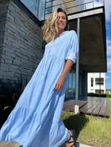 Vestido camisero largo celeste con rayas verticales blancas, cuello camisero, manga larga con puño y abotonadura frontal. Diseño escalonado con volantes en cada corte.