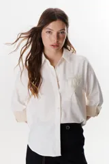 Camisa verde militar de manga larga con puños color crema, cuello clásico y cierre frontal con botones. Tiene un bolsillo en el pecho con bordado de una palmera color crema.