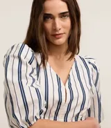 Blusa de sarga a rayas verticales blancas y azules, con cuello en V, mangas cortas abullonadas, lazo en la cintura y volado en el bajo.