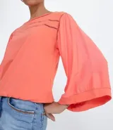 Blusa color salmón con escote redondo, mangas 3/4 amplias y ajuste frontal. Confeccionada en tejido laise.