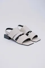 Sandalias bajas color crema con tres tiras en la capellada, una de ellas con textura tipo piel de cocodrilo. Pulsera con hebilla para ajustar al tobillo y taco cuadrado color negro.