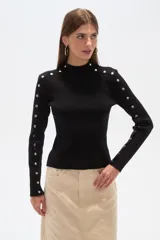 Sweater negro de punto con cuello alto y botones metálicos decorativos en hombros y mangas largas.