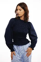 Blusa blanca de algodón con frunces tipo smock en el cuerpo, cuello redondo y mangas largas abullonadas con puños elásticos.