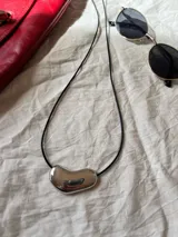Collar con cadena fina negra y dije plateado con forma irregular.