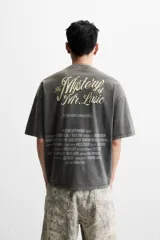 Camiseta gris oscuro con efecto lavado, cuello redondo y manga corta. Tiene un bolsillo en el pecho y estampados en el frente y la espalda.