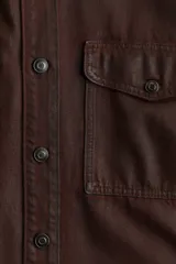 Sobrecamisa marrón de sarga de algodón revestida con cuello, botones adelante y canesú con pliegue de caja en la espalda. Modelo de corte holgado con hombros caídos, mangas largas con puños abotonados y bolsillos superiores con solapa y botón. Bajo redondeado y espalda algo más larga.