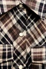 Vestido largo tipo camisero con estampado de cuadros en tonos marrón, negro y blanco. Tiene cuello solapa, mangas largas con puños abotonados, dos bolsillos de parche con solapa en el pecho y cierre frontal con botones a presión.