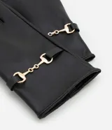 Par de guantes negros de cuero sintético con detalle de costuras en los dedos y tira ajustable con botón a presión en la muñeca.
