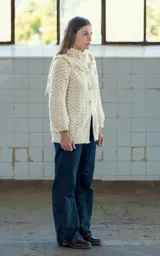 Cardigan tejido a crochet en lana merino color crudo, con volados dobles en hombros y cuello, canesú con tejido abierto y ajuste frontal con cuatro botones de guampa tallados a mano.