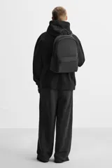 Mochila negra con acabado engomado, compartimento principal con cierre de cremallera, bolsillo interior con cierre, bolsillo frontal con cierre, bolsillos laterales planos, respaldo acolchado con sujeción para equipaje, asa de mano y dos asas de hombro ajustables y acolchadas.