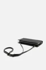 Bandolera negra rectangular con textura grabada. Tiene un compartimento principal con cierre de cremallera, un bolsillo interior con cremallera y un bolsillo simple. El asa de hombro es ajustable y extraíble.