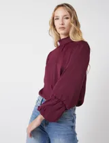 Blusa de gasa satén color bordó, marca Tahari, con cuello alto fruncido y mangas largas abullonadas. La espalda tiene una abertura central con botón.