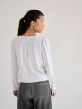 Remera blanca de algodón con escote redondo, mangas largas y pespuntes verticales a contratono.