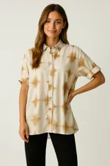 Camisa color crema con estampado abstracto en tonos marrones, de corte holgado, manga corta con dobladillo, cuello camisero y cierre frontal con botones.