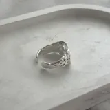Anillo de diseño abstracto y plateado, con textura irregular.
