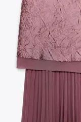 Vestido midi color lila, de cuello halter y sin mangas. La parte superior es de tejido arrugado y la falda es plisada. Tiene abertura en la espalda con cierre de botones ocultos.