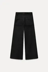 Pantalón ancho de pana color negro, de tiro medio, con trabillas en la cintura, bolsillos delanteros y cierre frontal con cremallera, botón y gancho metálico.