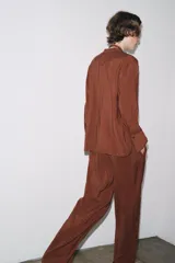 Camisa marrón de Zara Woman Collection confeccionada en hilatura con mezcla de lyocell. Tiene cuello redondo, manga larga acabada en puño, bajo asimétrico con aberturas laterales y cierre frontal con botones.