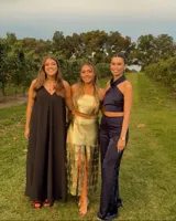 Conjunto de dos piezas de cuero color dorado, compuesto por un top estilo bandeau y una falda midi con abertura frontal y flecos metálicos colgantes.