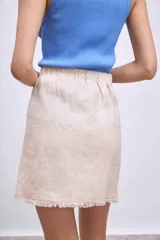 Minifalda color beige de corte evasé con diseño cruzado y detalle de flecos en el ruedo.