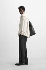 Camisa color crema de corte relaxed fit, confeccionada en tejido de mezcla de algodón suave al tacto. Tiene cuello solapa, manga larga con puños abotonados, un bolsillo de parche en el pecho y cierre frontal con botones.