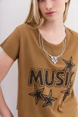 Remera color camel de mangas cortas confeccionada en jersey de algodón, de calce al cuerpo y escote redondo en punto rib a tono. Cuenta con una estampa central al agua de efecto desgastado con la palabra "Music" y estrellas, y un aplique de cadenas y piedras que simula ser un collar.