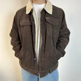 Chaqueta marrón de pana con cuello y forro de corderito color crema, cierre con botones y bolsillos frontales con solapa.