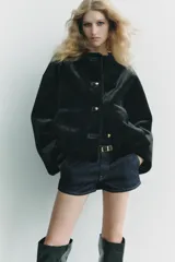 Chaqueta corta de cuello redondo y manga larga en tejido de pelo sintético color negro. Cierre frontal con botones metálicos dorados y bolsillos de plastrón. Colección Zara Woman.
