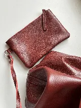 Cartera tipo tote bag color bordó, confeccionada en cuero con textura granulada. Tiene doble asa corta de mano y asa larga extraíble con diseño de tachas para usar como bandolera.