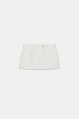 Falda pantalón corta color blanco, de tiro bajo, con bolsillos delanteros y cierre frontal con cremallera y botón joya.