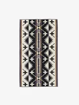 Toalla extragrande de felpa suave con acabado aterciopelado en un lado y diseño de bucles en el otro. Presenta un patrón geométrico en blanco y negro con franjas laterales en tonos marrones y grises.