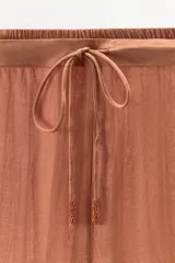 Pantalón marrón de tiro alto con cintura elástica ajustable con lazada, corte palazzo y detalle de bordados en forma de rombo y puntilla a tono en el ruedo y laterales.