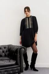 Minivestido negro de viscosa con corte en la cintura, detalles de puntillas en cuello y ruedo, gota en la espalda y pechera bordada en hilo con apliques.