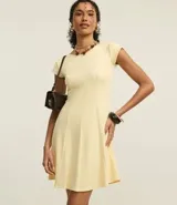 Vestido corto color amarillo pálido, con cuello redondo, mangas cortas y corte acampanado en la falda. Presenta recortes verticales en el torso que definen la silueta.