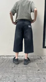 Bermuda de jean negra de corte ancho (baggy) y largo 3/4, con bordados de estrellas blancas en la parte inferior de la pierna izquierda.