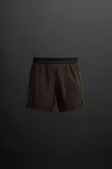 Shorts deportivos color marrón confeccionados en tejido técnico ligero y elástico. Cuenta con cintura elástica ajustable con cordón interior, bolsillos frontales, bolsillo trasero con cierre de cremallera, forro interior y bajo con aberturas laterales.