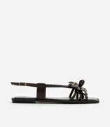 Sandalia plana color marrón con punta cuadrada, tiras finas con flor central y strass, y cierre de tira fina con hebilla cuadrada.