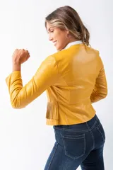 Chaqueta corta de cuero sintético color mostaza, con cuello camisero blanco, cierre frontal con cremallera y detalle de flecos en el ruedo.