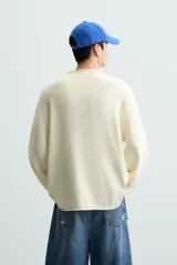 Jersey color crudo de algodón con textura, corte relaxed fit, cuello redondo y manga larga. Acabados en rib con detalle de vuelta.