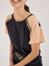 Remera negra de algodón con mangas cortas con detalle de calado y bordado en los hombros y mangas. Corte recto con cintura ajustable con cordón.