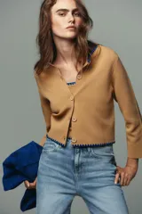 Chaqueta color mostaza de punto liso con cuello redondo y manga larga. Detalle de bordados a contraste en cuello y ruedo. Cierre frontal con botones.