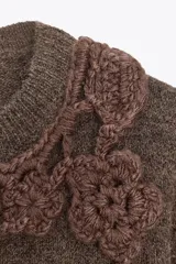 Sweater marrón de tejido de punto con cuello redondo y mangas cortas. Presenta apliques florales tejidos al crochet en el frente.
